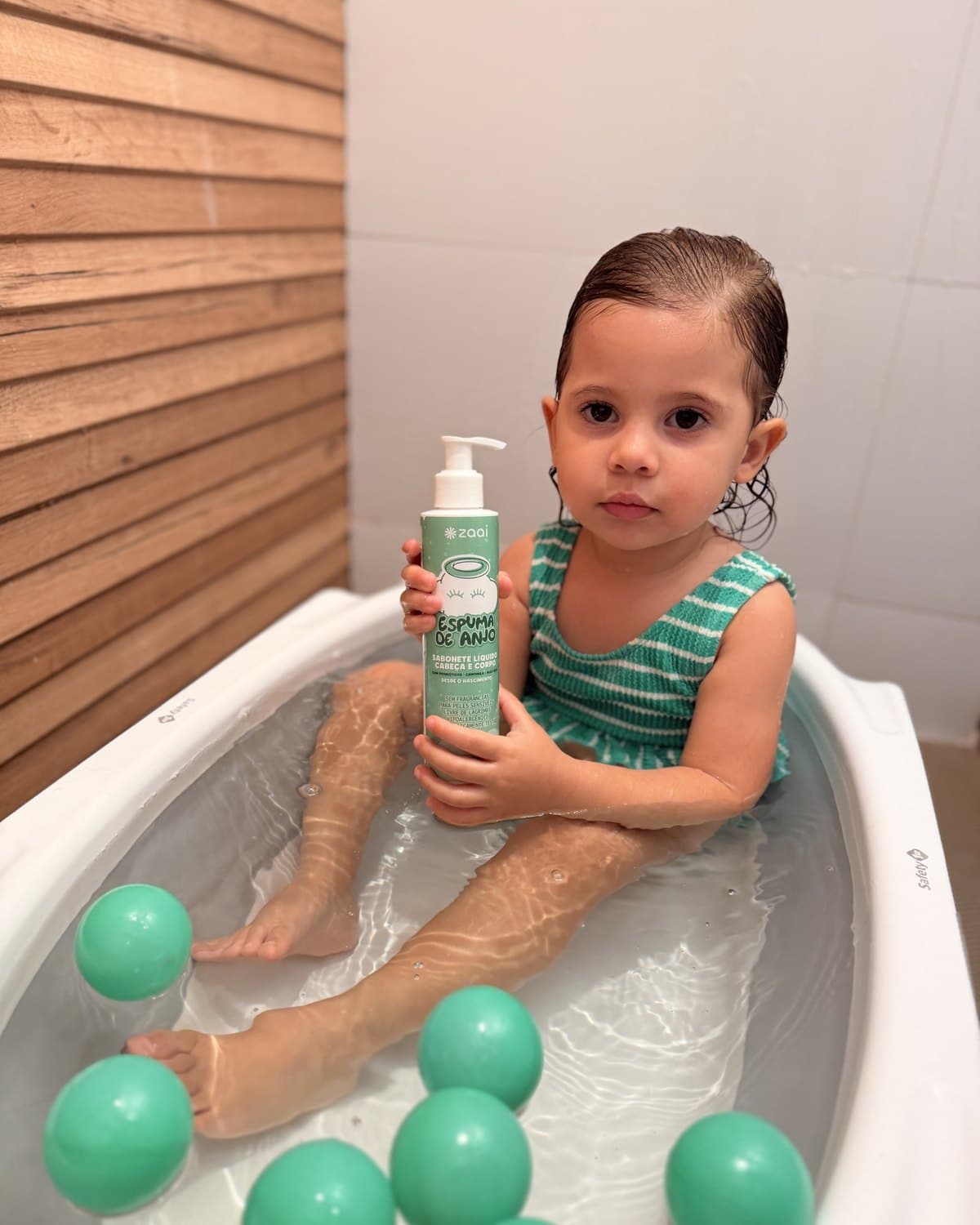 Criança sentada na banheira segurando o frasco da Espuma de Anjo